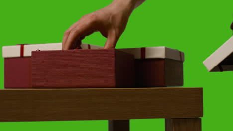 Close-Up-Of-Man-Opening-Gift-Wrapped-Present-On-Table-Shot-Against-Green-Screen-1